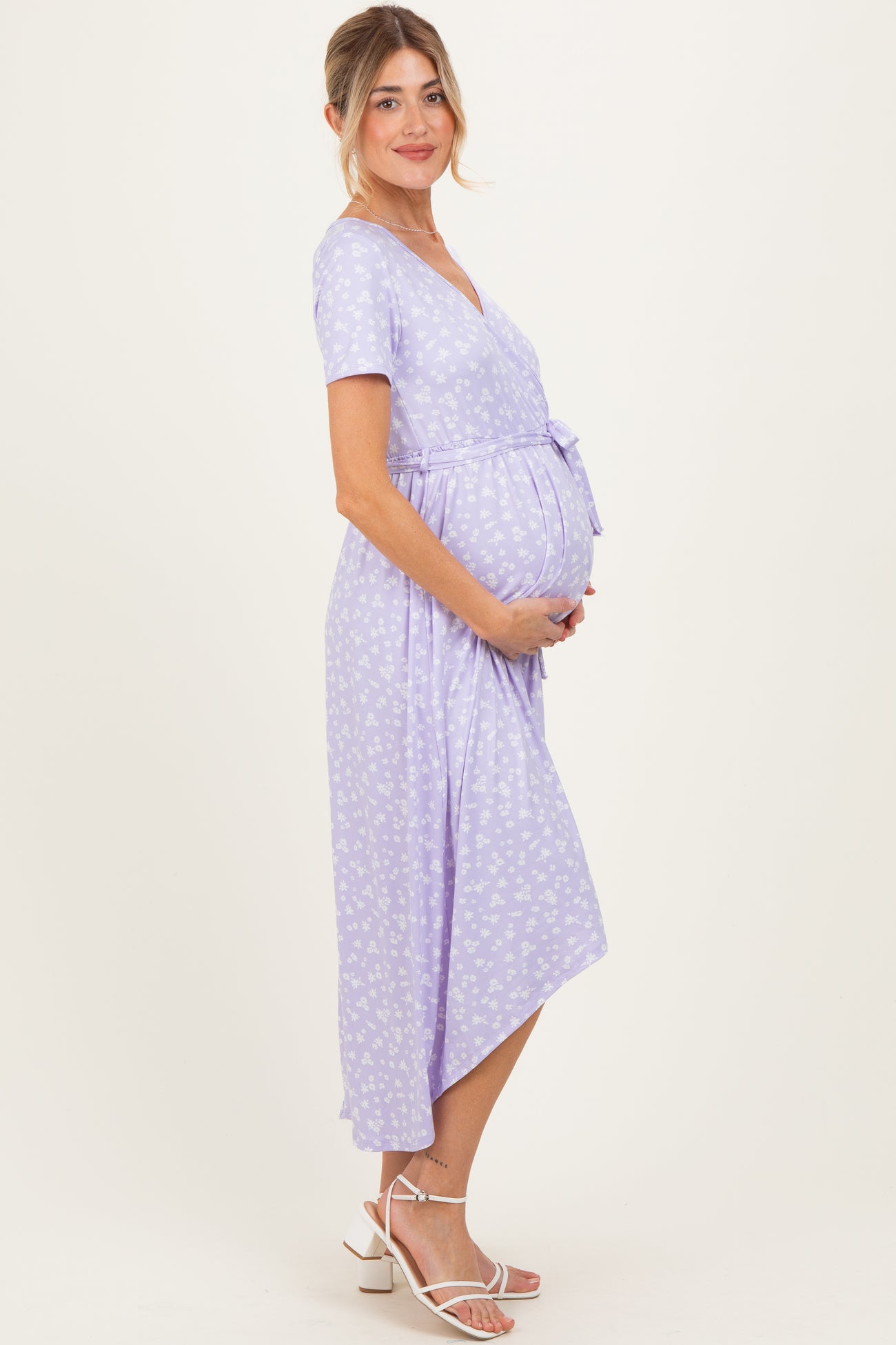 woman wearing a lilac floral wrap maternity dress and holding her baby bump