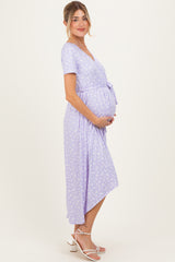woman wearing a lilac floral wrap maternity dress and holding her baby bump