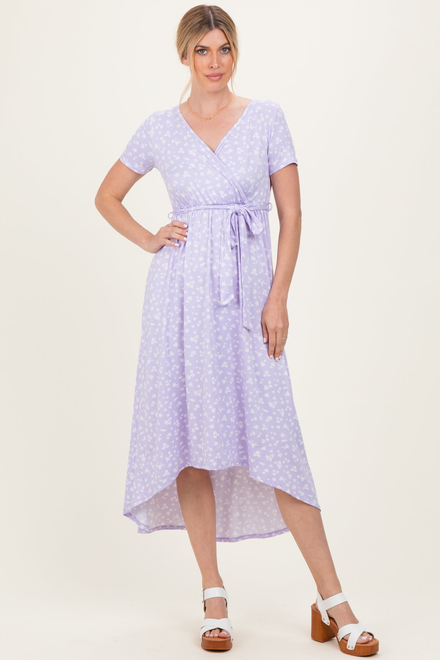 woman wearing a lavender wrap dress with short sleeves and a high-low hem, styled with white block-heel sandals