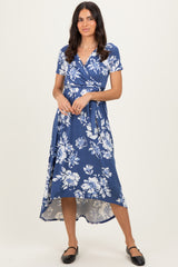 woman wearing a blue floral wrap dress with short sleeves and a high-low hemline, standing and smiling