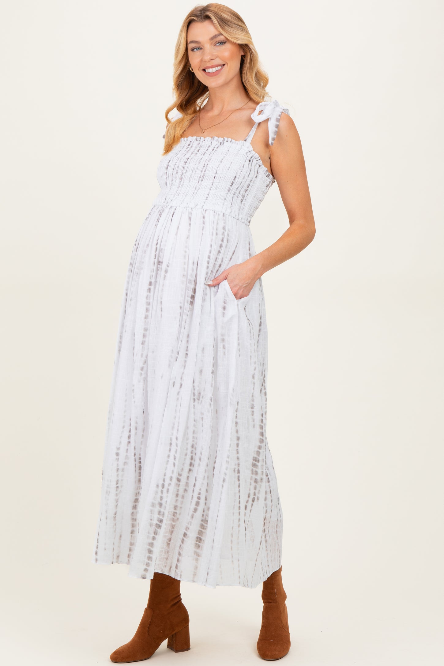 woman wearing a white and gray striped maternity maxi dress with smocked bodice and side pockets, showcasing her baby bump