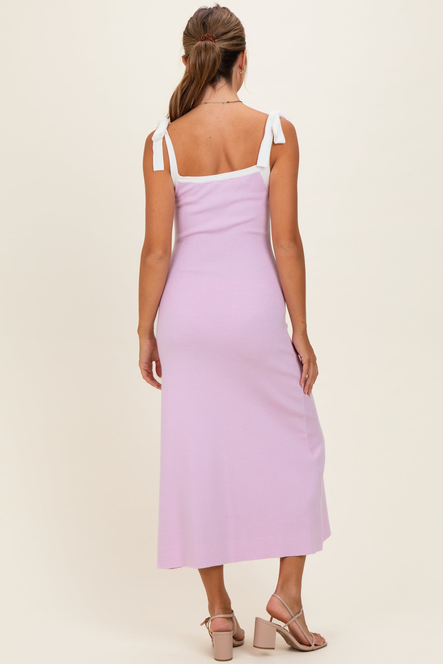woman wearing a lilac backless midi dress with white tie straps and styled with beige heeled sandals