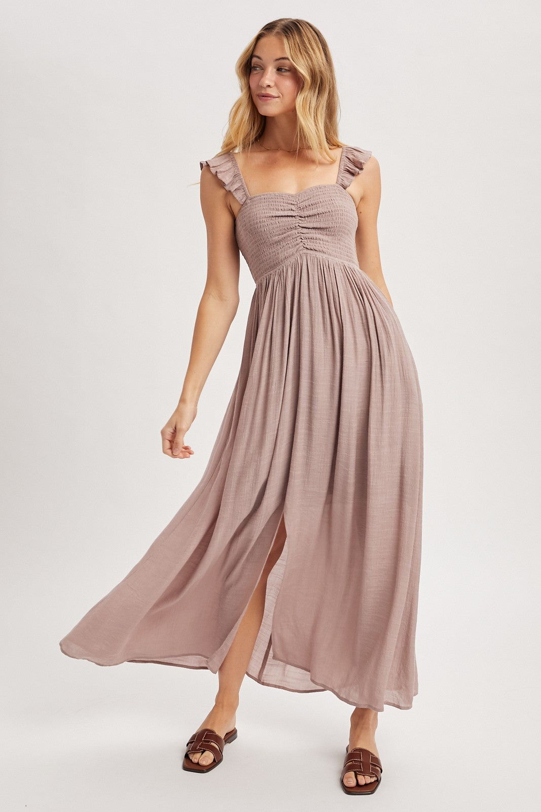 woman wearing a light mauve sleeveless maxi dress with ruffled straps and a front slit