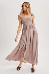 woman wearing a light mauve sleeveless maxi dress with ruffled straps and a front slit