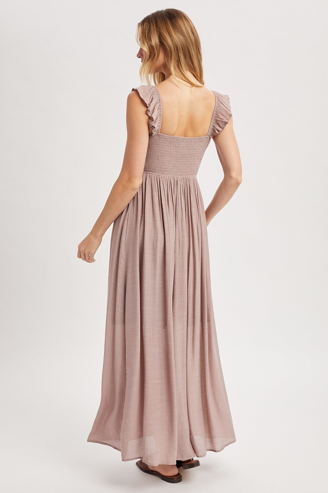 woman wearing a dusty rose long maxi dress with ruffle sleeves and a smocked bodice, viewed from the back