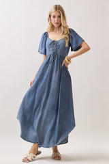 woman wearing a blue denim maxi dress with short puff sleeves and a lace-up front detail