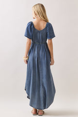 woman wearing a denim maxi dress with short puff sleeves and an elastic waist, viewed from the back