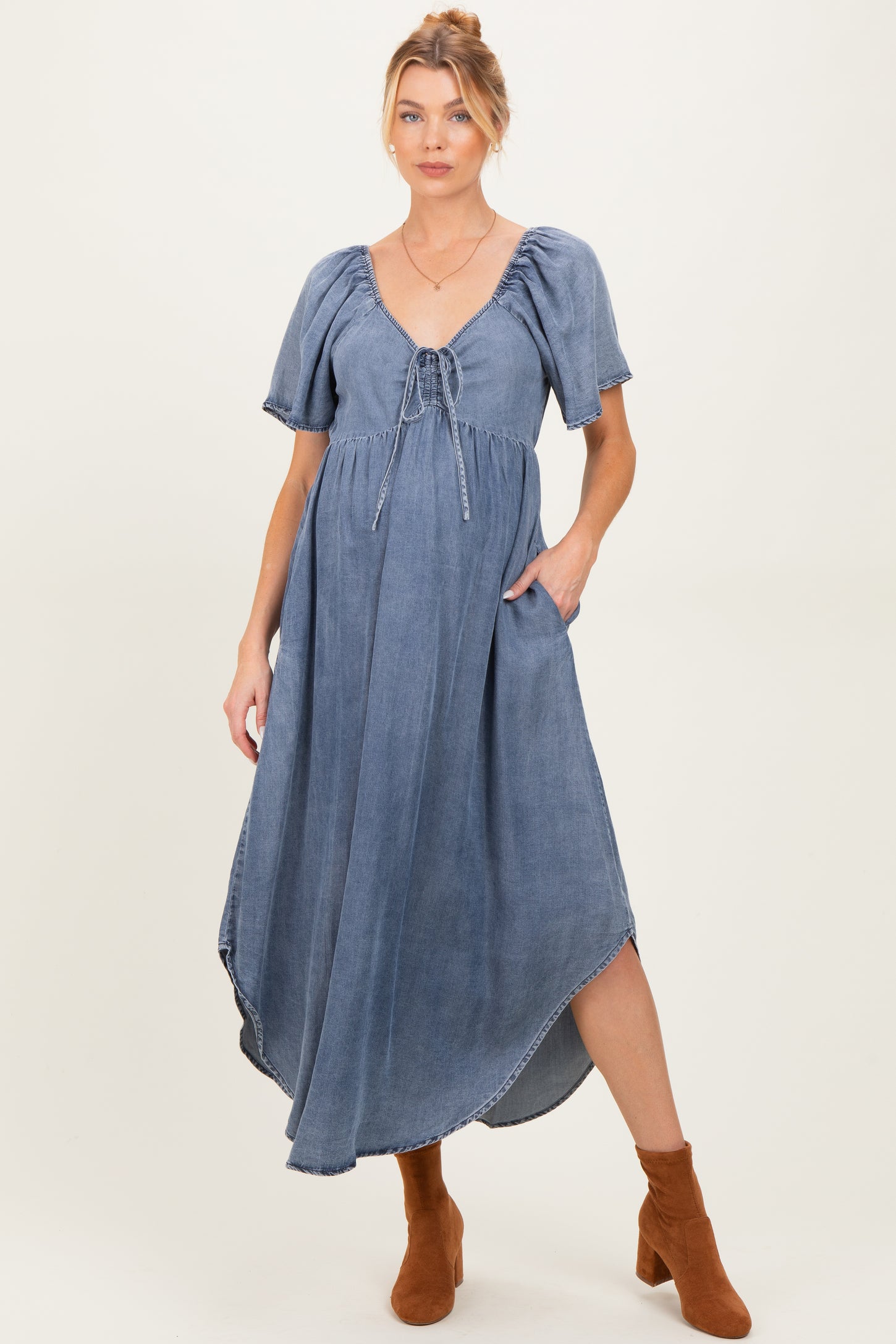 woman wearing a denim maternity dress with short puff sleeves and a drawstring waist, and holding her baby bump