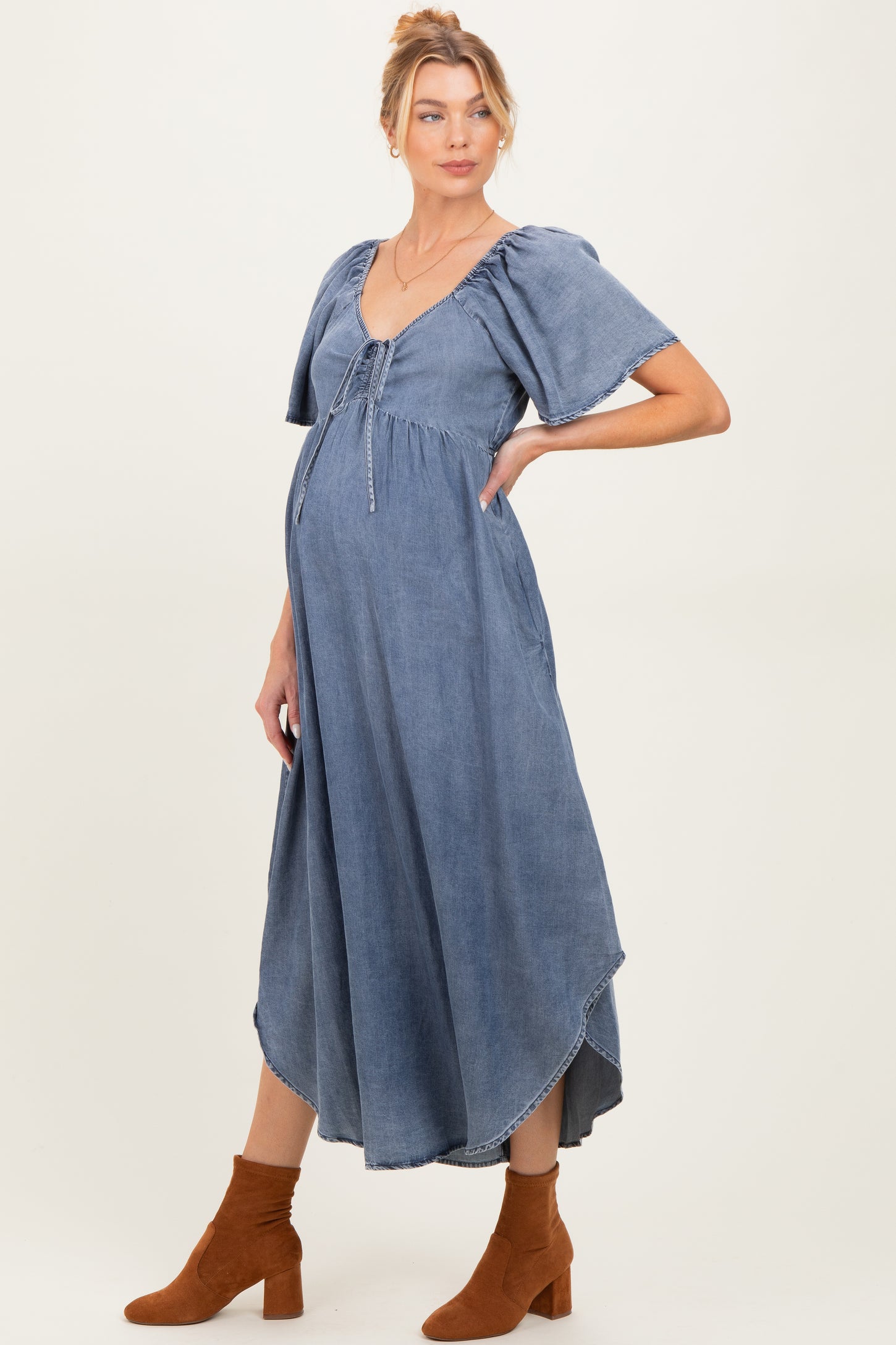 woman wearing a blue denim maternity dress with flutter sleeves and a baby bump visible