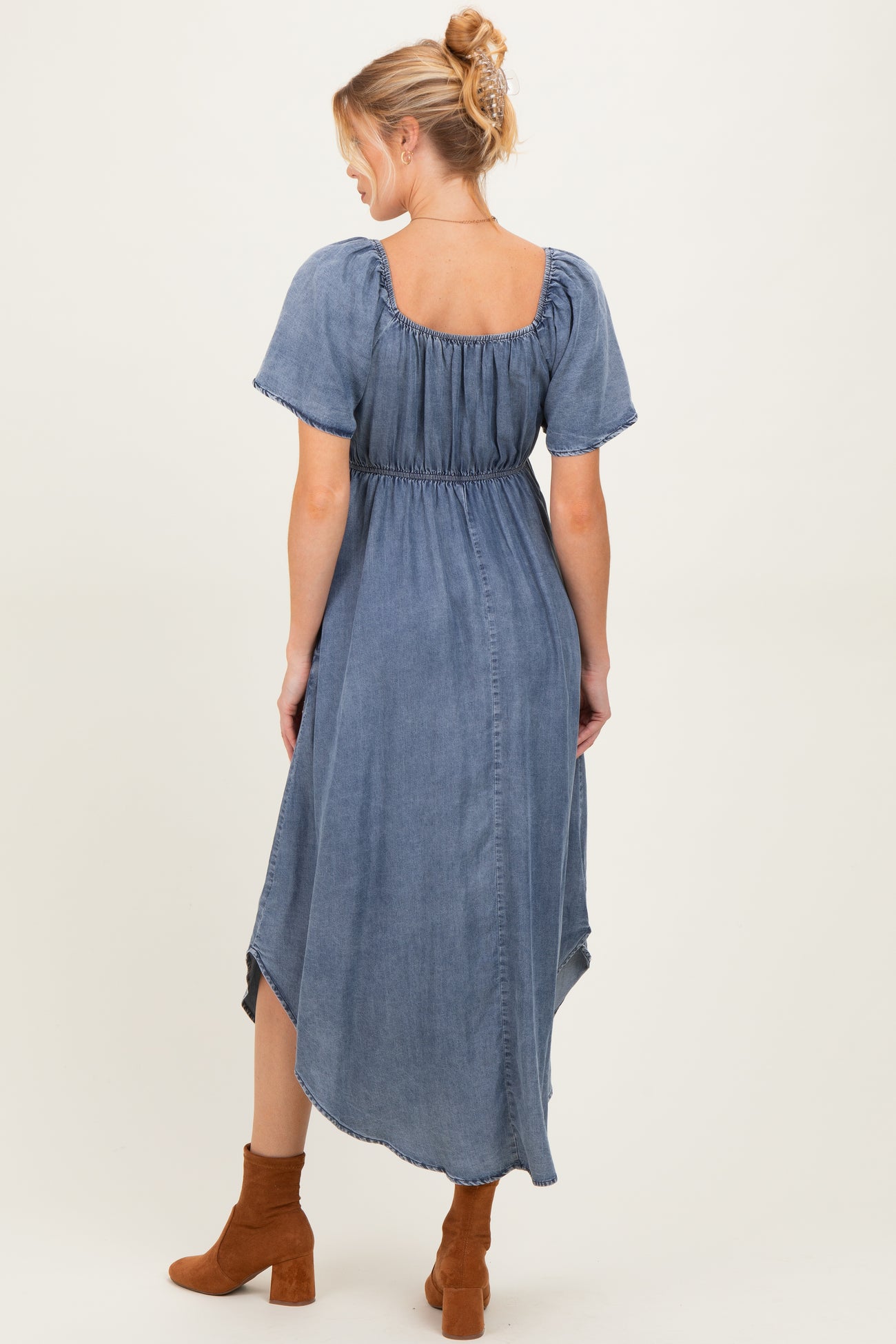 woman wearing a blue denim maternity dress with short puff sleeves and a high-low hemline, showing off her baby bump