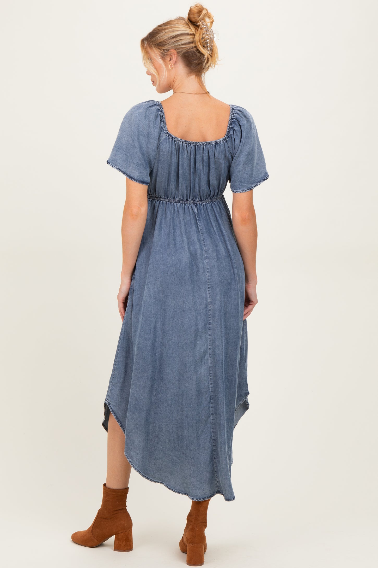 woman wearing a blue denim maternity dress with short puff sleeves and a high-low hemline, showing off her baby bump