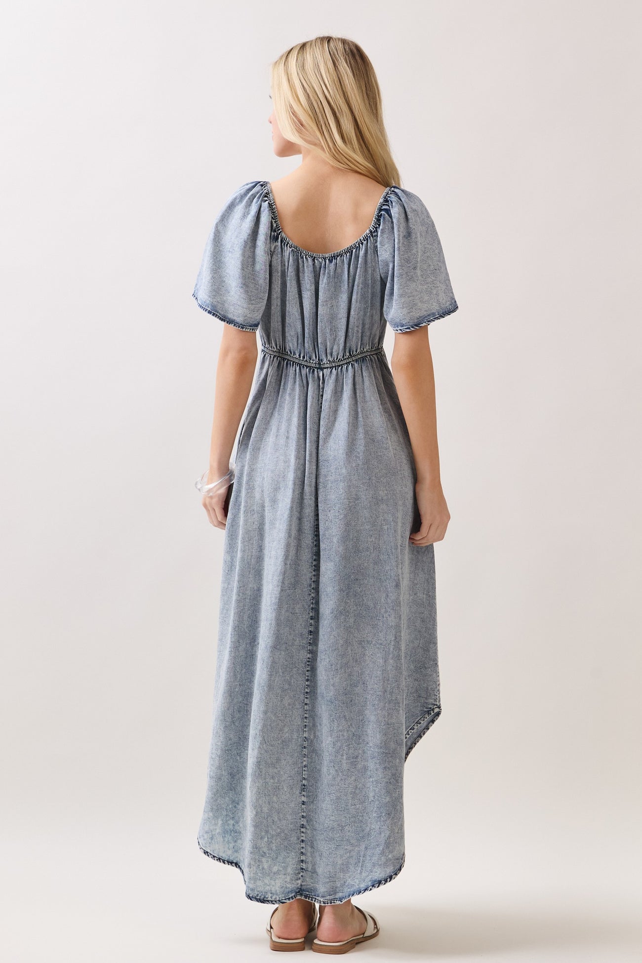 woman wearing a light blue puff sleeve maxi dress with a cinched waist and a flowy skirt, standing with her back to the camera