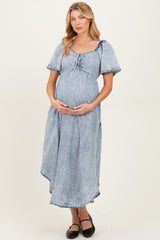 woman wearing a light blue denim maternity dress with a tie detail and holding her baby bump
