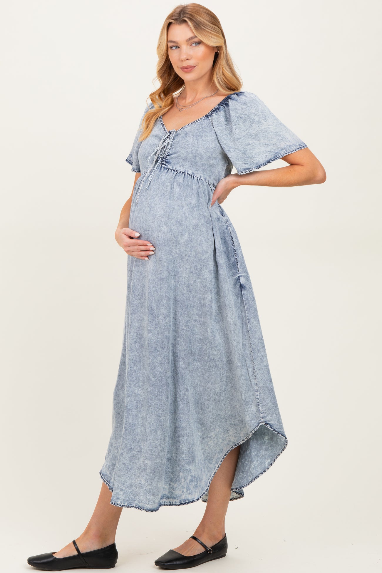 woman wearing a light blue denim maternity dress with short sleeves and a gathered waist, showcasing her baby bump