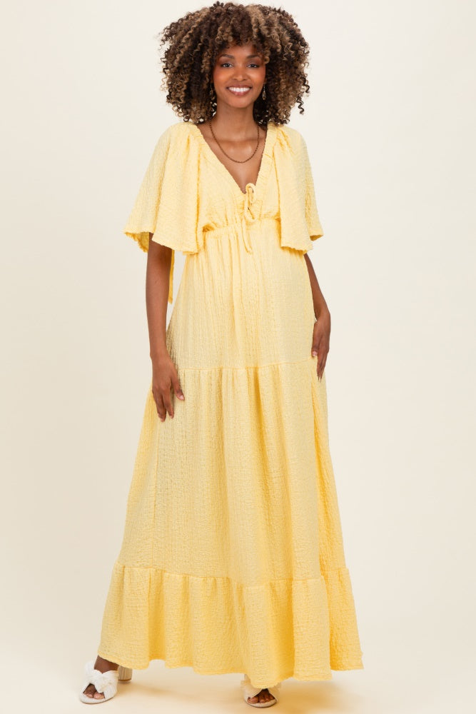 woman wearing a yellow maternity maxi dress with flutter sleeves and a tie front detail, showcasing a baby bump