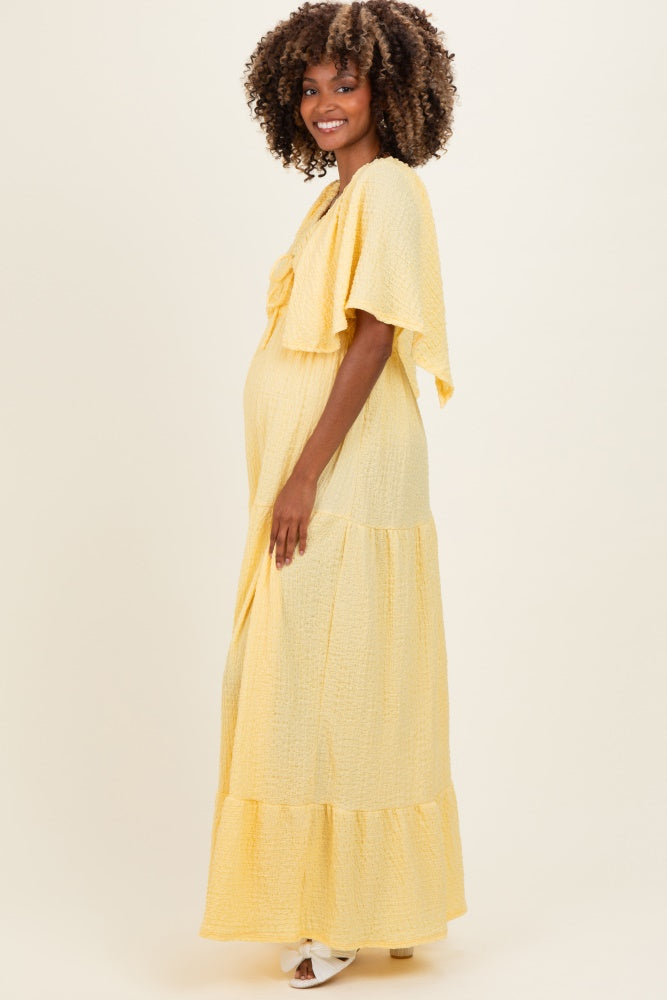 woman wearing a light yellow maternity maxi dress with flutter sleeves and a tiered skirt, showcasing her baby bump