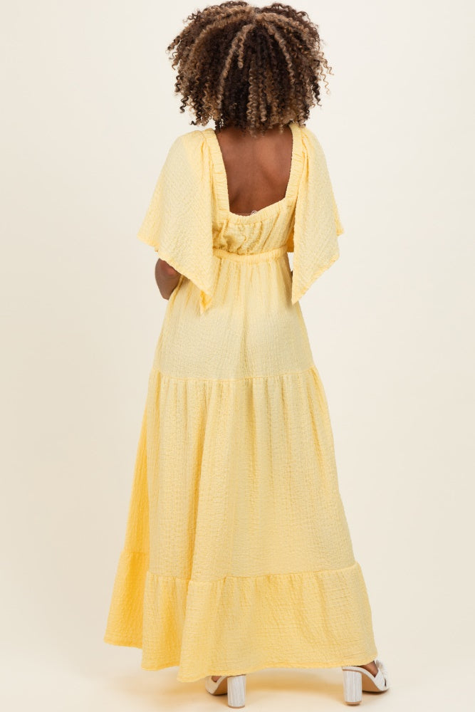 woman wearing a yellow maternity maxi dress with flutter sleeves and tiered ruffle hem, viewed from the back
