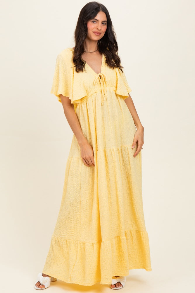 woman wearing a yellow tiered maxi dress with short sleeves and a tie detail at the neckline