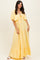 woman wearing a yellow tiered maxi dress with short sleeves and a tie detail at the neckline