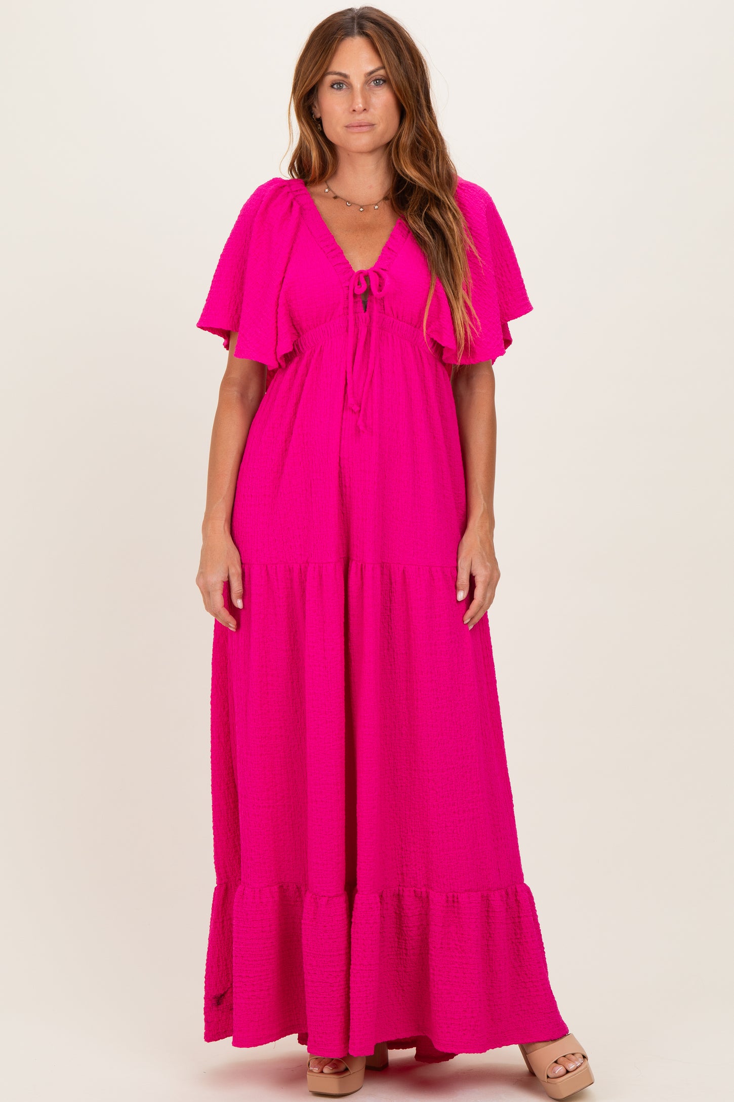 woman wearing a bright pink maxi dress with flutter sleeves and tie detail at the neckline