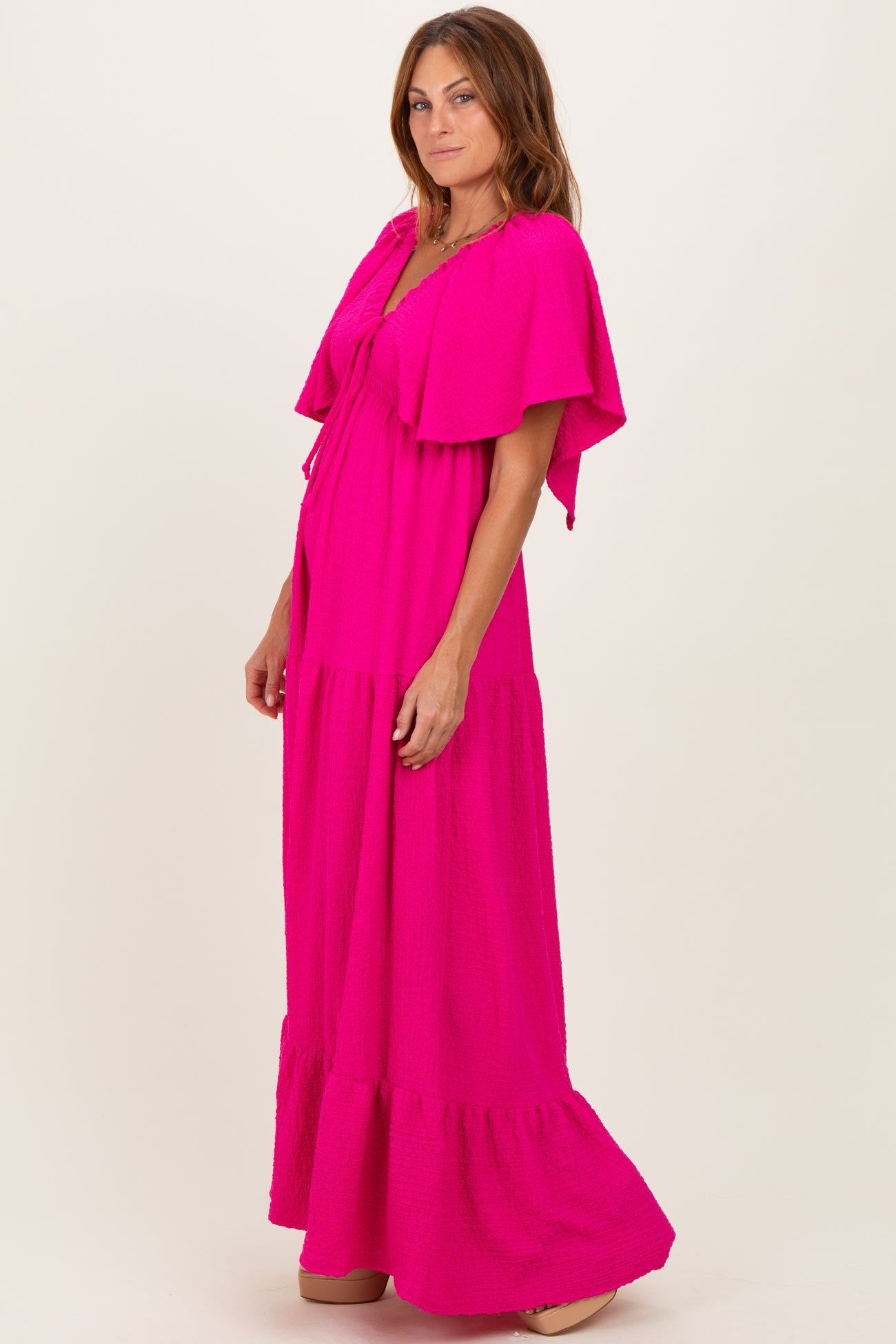 woman wearing a bright pink maxi dress with flutter sleeves and a tiered bottom