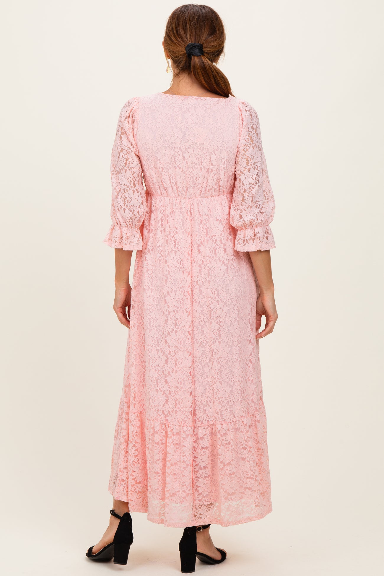 woman wearing a light pink lace maxi dress with puff sleeves and a tiered hem, viewed from the back
