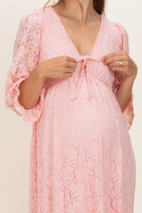 woman wearing a light pink lace maternity dress with a tie detail at the neckline and a visible baby bump