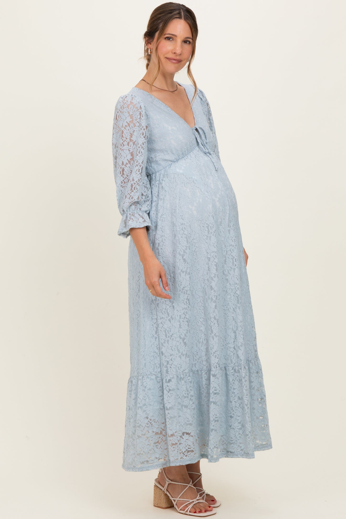 woman wearing a light blue lace maternity dress with a bow detail and a flowing silhouette, showing her baby bump