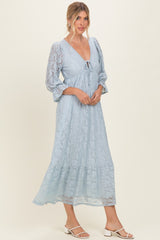 woman wearing a light blue lace maxi dress with puff sleeves and a tie detail at the neckline