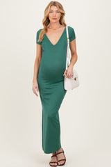 woman wearing a green maternity maxi dress with a deep v-neck and short sleeves, holding a white handbag, showcasing her baby bump