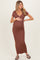 woman wearing a brown v-neck maternity maxi dress with a side slit and holding her baby bump