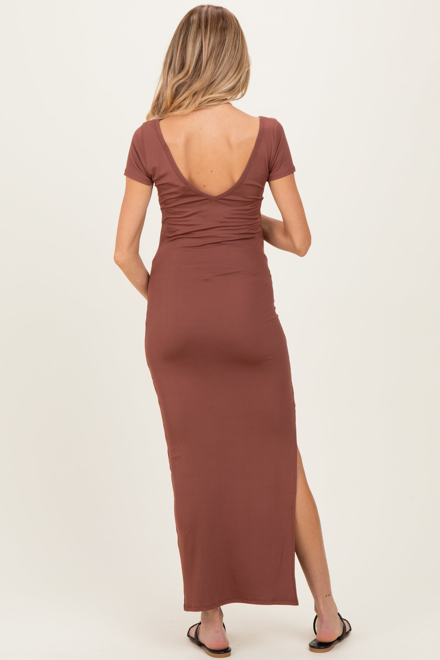 woman wearing a brown maternity maxi dress with a ruched back and a side slit, showing a pregnant belly