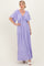 woman wearing a lavender maxi dress with flutter sleeves and a tie neckline, standing against a plain background