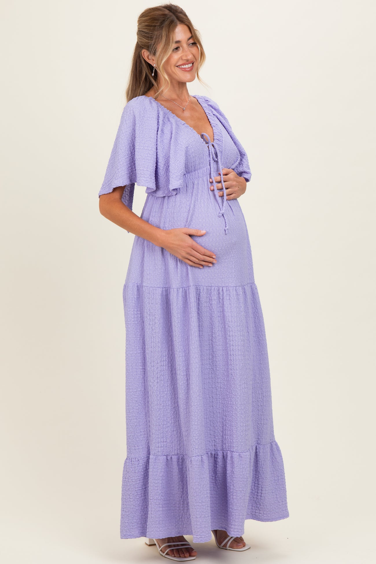woman wearing a lavender maternity maxi dress with short sleeves and a tie-front detail, holding her baby bump