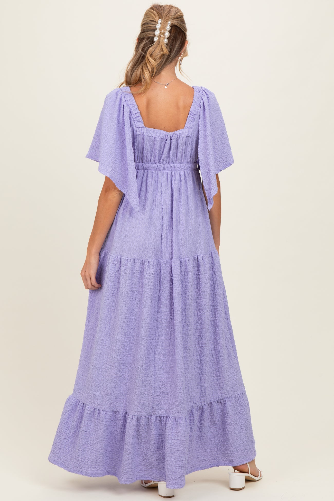 woman wearing a lavender maternity maxi dress with flutter sleeves and tiered ruffle details, viewed from the back