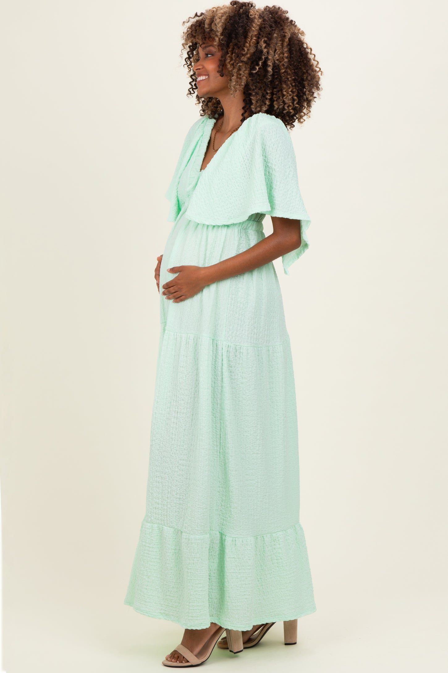 woman wearing a mint green maxi maternity dress with flutter sleeves and a visible baby bump