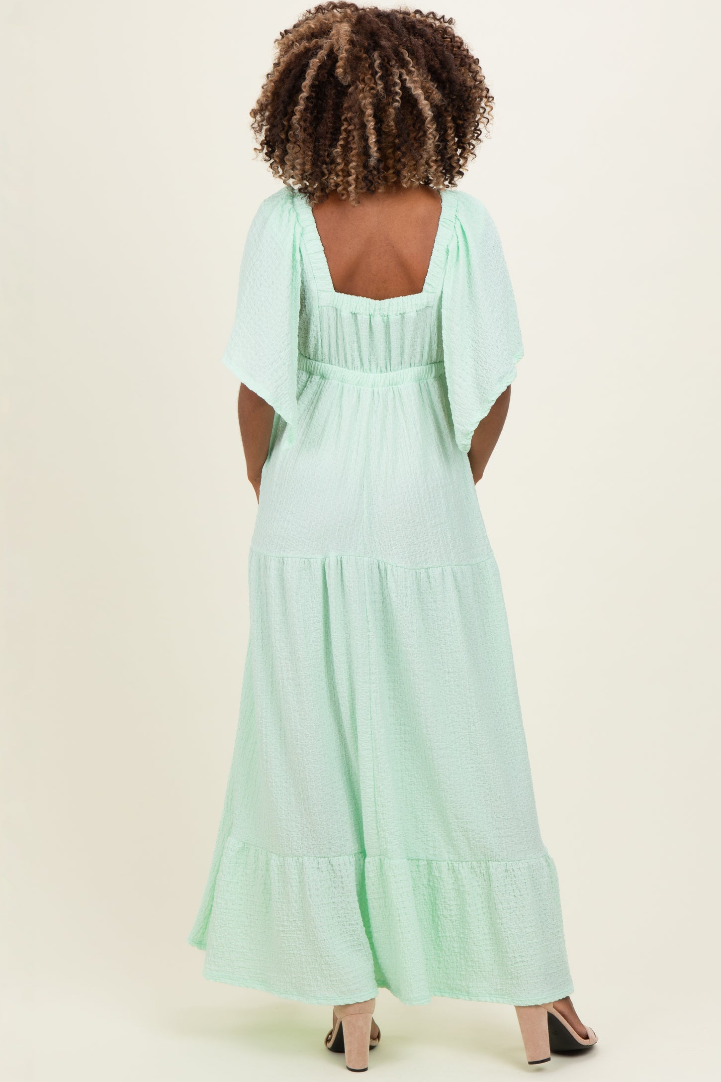 woman wearing a light green maternity maxi dress with flutter sleeves, showing the back view and a flowing silhouette