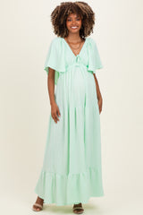 woman wearing a mint green maternity maxi dress with flutter sleeves and a tie detail, showing her baby bump