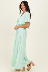 woman wearing a light green maxi dress with ruffle sleeves and tiered skirt, standing in profile