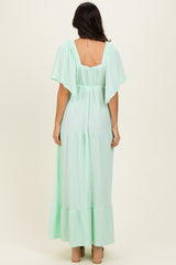 woman wearing a light mint green maxi dress with flutter sleeves and a tiered design, viewed from the back