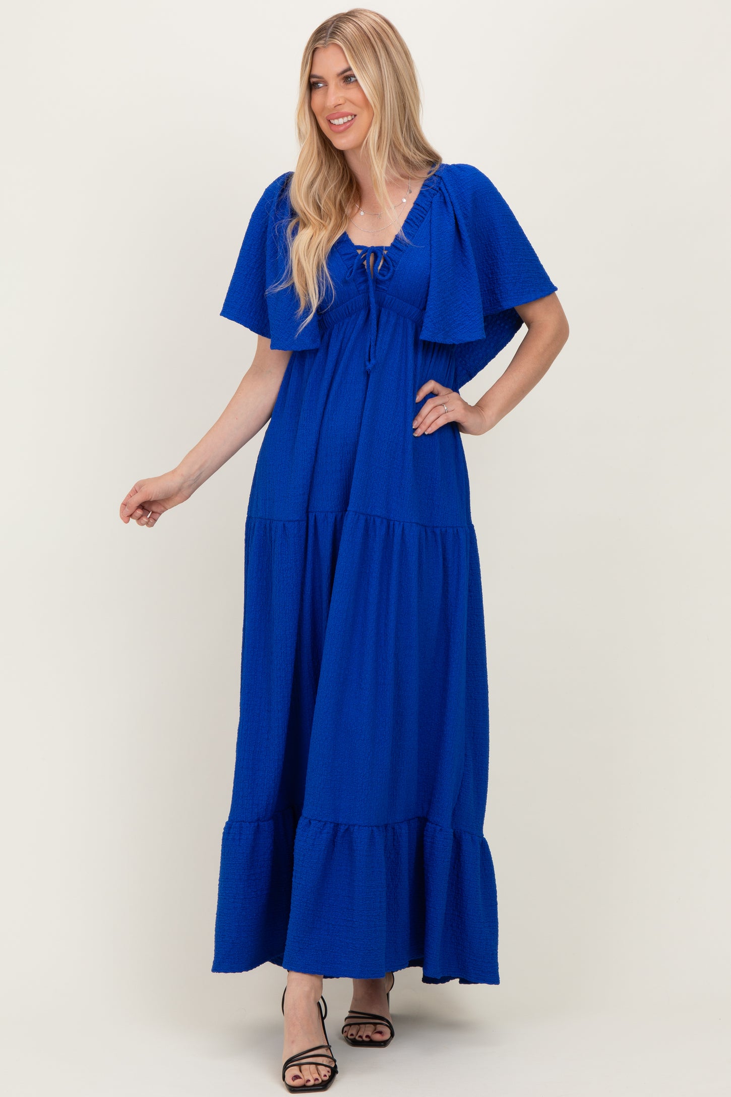 woman wearing a bright blue tiered maxi dress with flutter sleeves and drawstring neckline