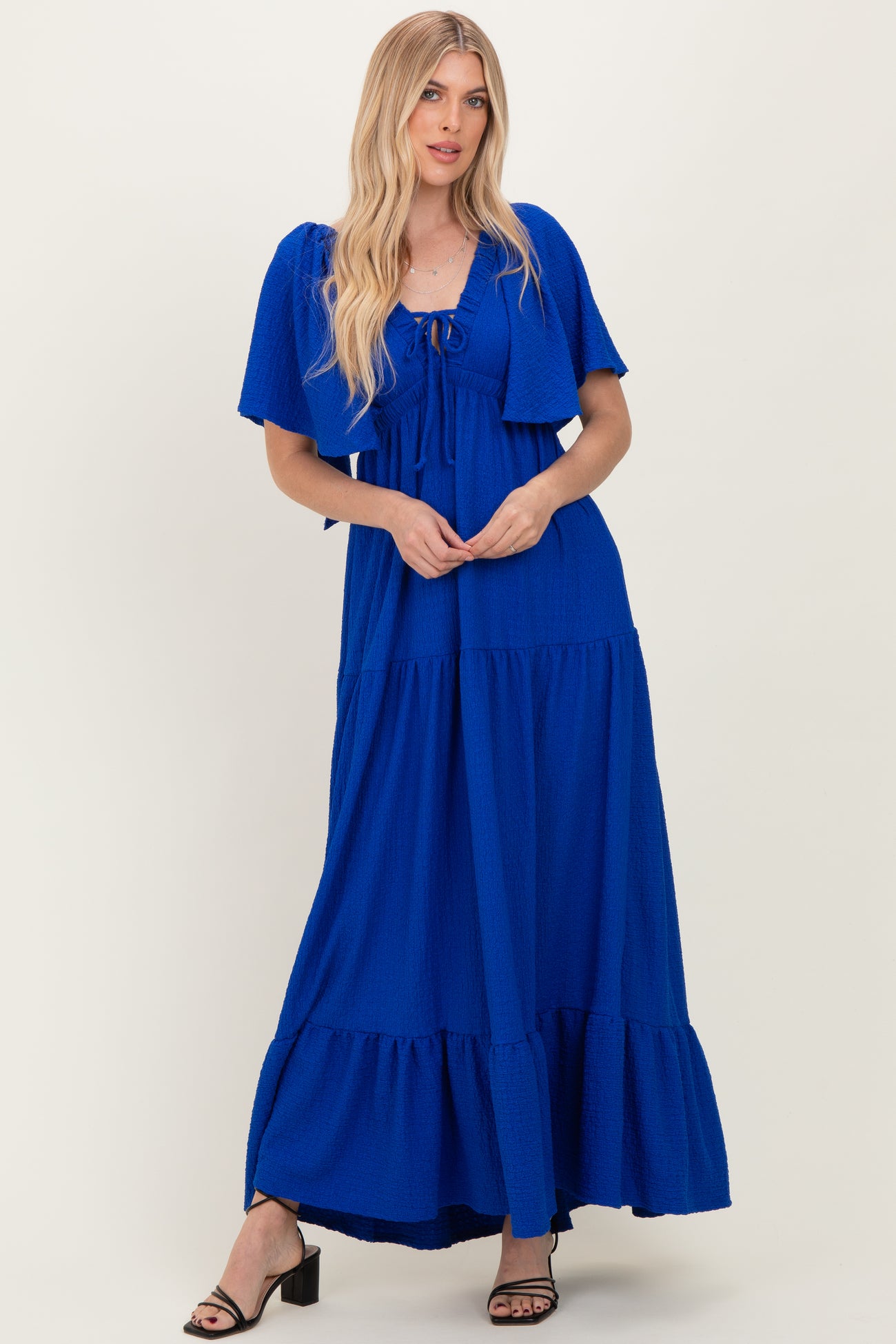 woman wearing a royal blue maxi dress with a tie-front top and tiered skirt, styled with a cropped cardigan