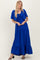 woman wearing a royal blue maxi dress with a tie-front top and tiered skirt, styled with a cropped cardigan