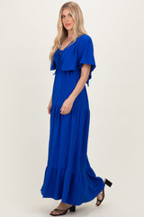 woman wearing a vibrant blue maxi dress with short sleeves and a tiered skirt, standing on a neutral background