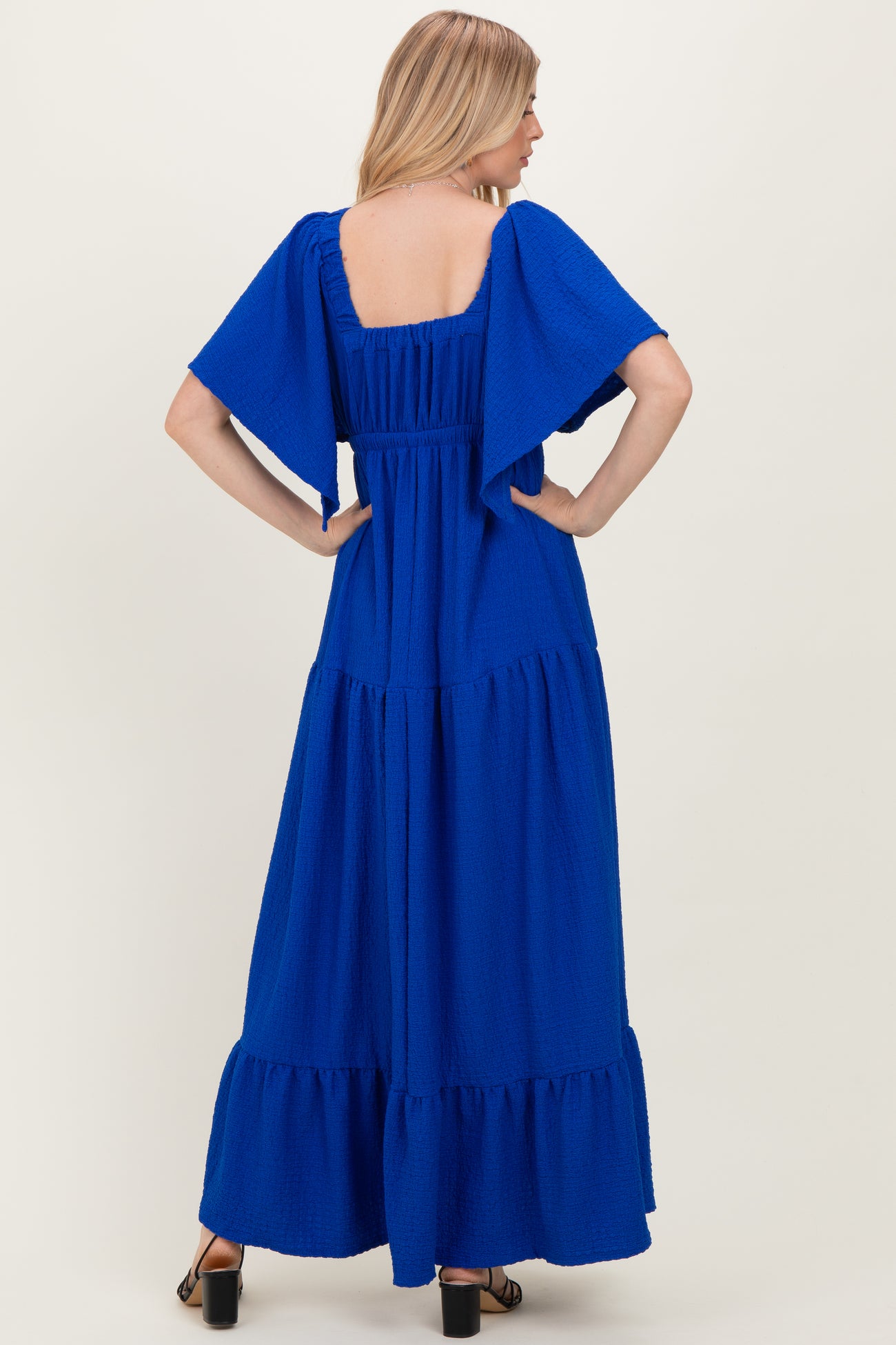 woman wearing a bright blue maxi dress with short flutter sleeves and tiered ruffle hem, seen from the back