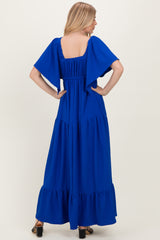 woman wearing a bright blue maxi dress with short flutter sleeves and tiered ruffle hem, seen from the back