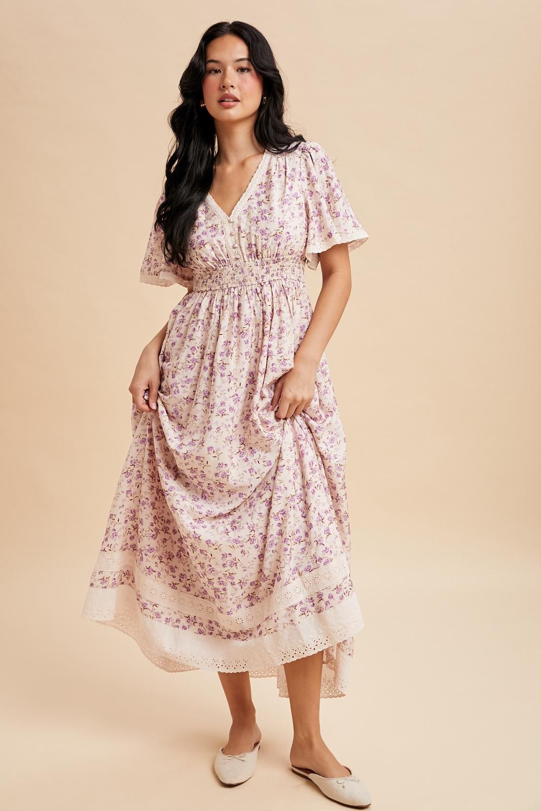 woman wearing a floral pink midi dress with ruffled sleeves and a gathered waist, standing on a beige background