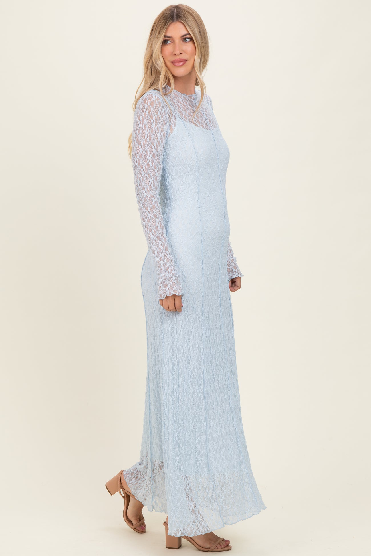 woman wearing a light blue long sleeve lace maxi dress with a fitted bodice and flared hem, styled with open-toed sandals