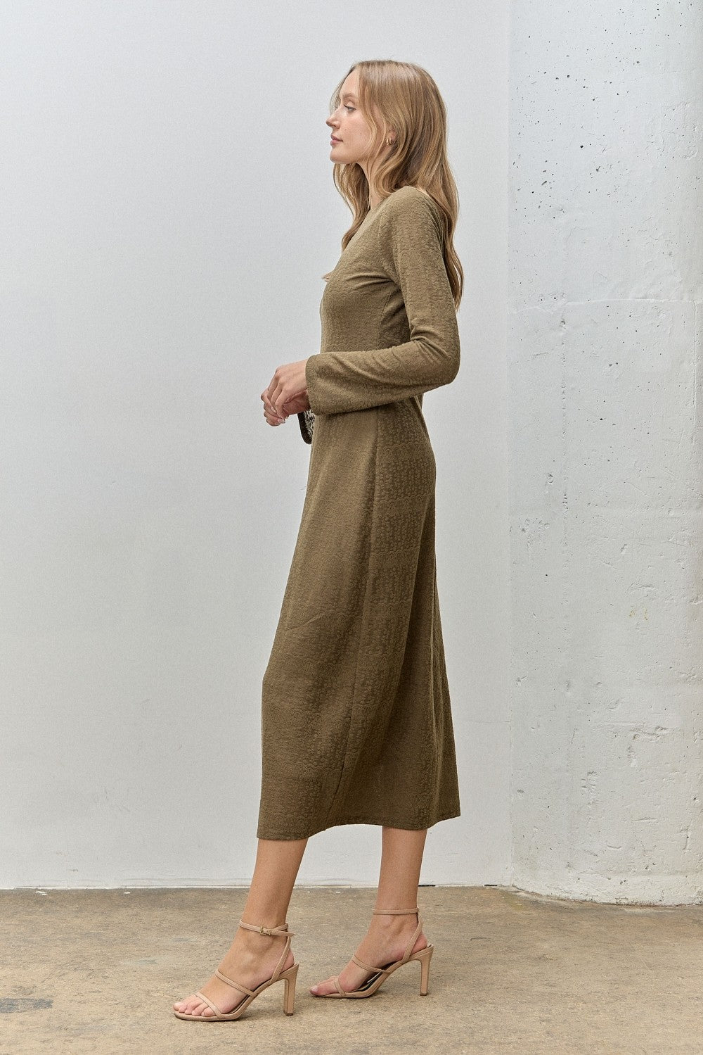 woman wearing a long sleeve olive green midi dress, standing sideways with strappy heels