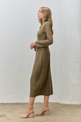 woman wearing a long sleeve olive green midi dress, standing sideways with strappy heels